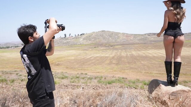 Hot Latina influencer in daisy dukes and cowboy hat poses for photographer in field shoot