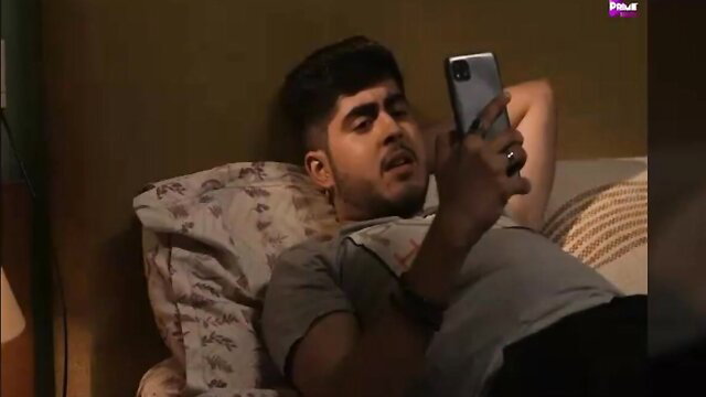 Handsome young Indian guy lounging shirtless on bed, checking phone