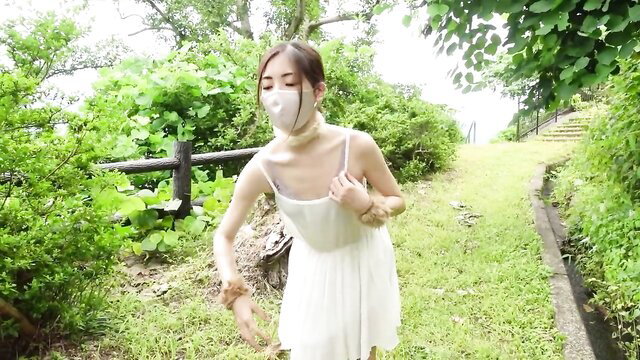 Asian girl in white dress and mask does pet play BDSM in lush mountains