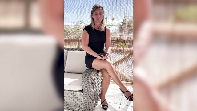 Laetitia 50 in tight black mini dress on sofa, hot legs