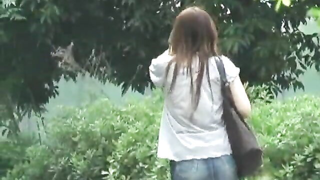 Asian teen in white blouse and tight jeans walks in lush green outdoors