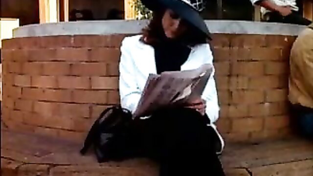 Brunette in white blazer and hat reading newspaper on bench in taboo porn thumbnail
