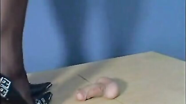 Woman in black stockings and stilettos crushing cock on table