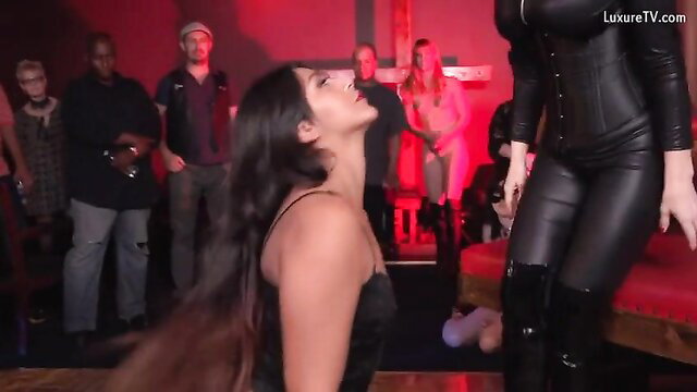 Dominatrix in leather corset stands over kneeling brunette sub in BDSM scene