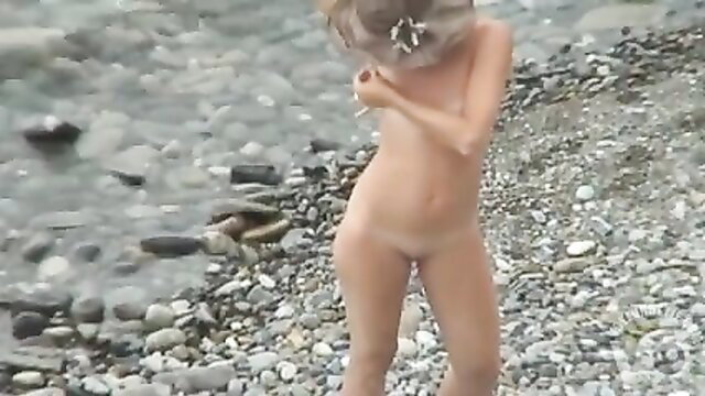 Nude blonde nudist girl relaxes naked on rocky beach alone