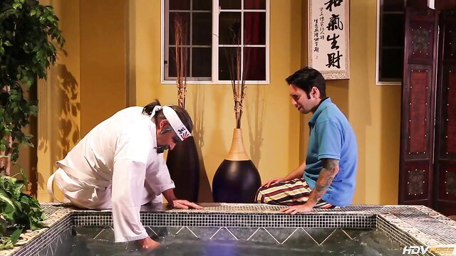 Asian men in hot tub at spa, one in chef uniform kneeling by pool