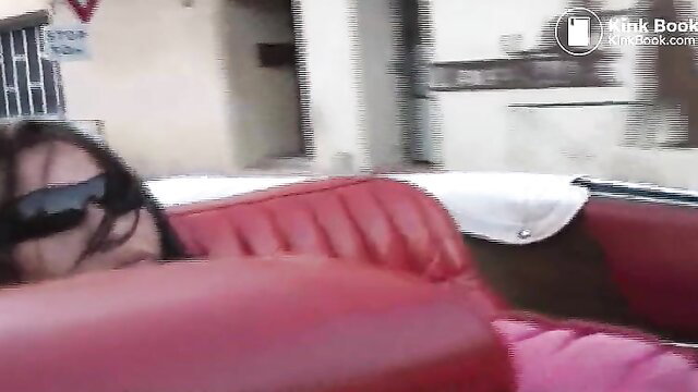 Latina woman in sunglasses reclining in red vintage car seat, public pantypoop tease