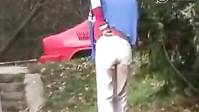 Woman in tight white pants with visible mess, bending over by red car outdoors
