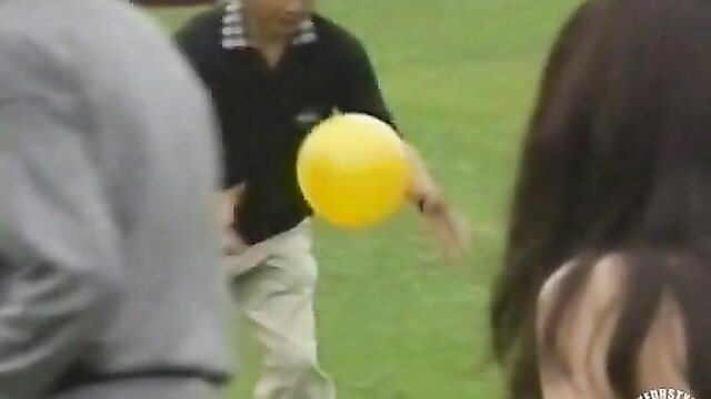 Amateur nude soccer game with Asian players tossing yellow ball outdoors