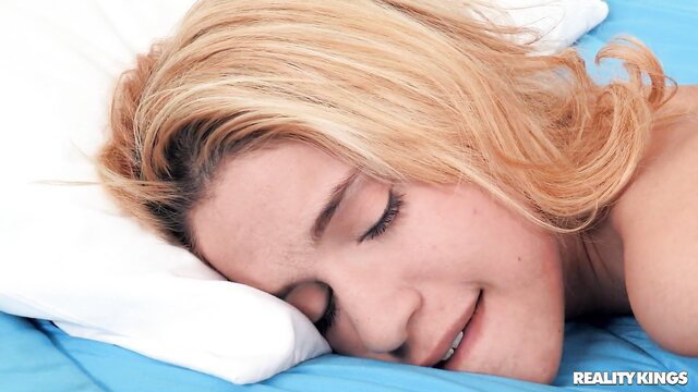 Cute blonde babe sleeping nude on blue sheets, smiling softly