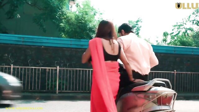 Indian beauty in red saree and black blouse rides pillion on scooter with man