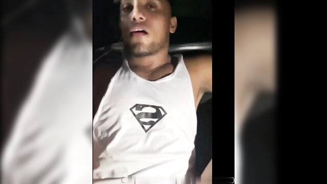 Mixed-race man in Superman tank top leans back in car, seductive gaze