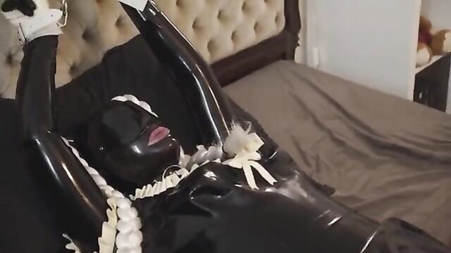 Shiny black latex doll restrained in bondage on bed