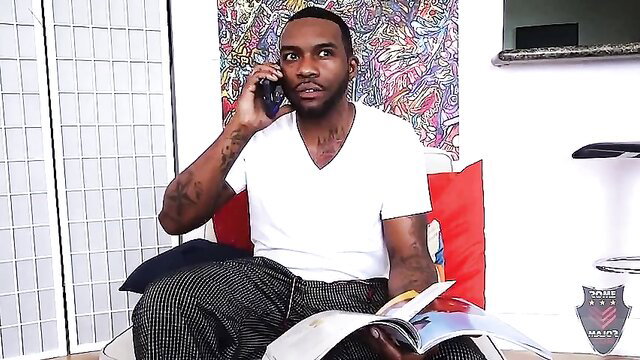 Rome Major on phone in white V-neck, gray pants, holding magazine