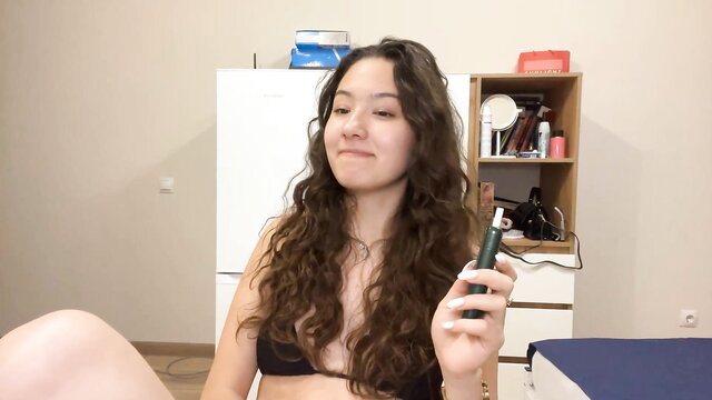 Kelikurtulus in black bikini top, wavy hair, teasing with green toy