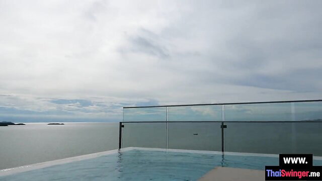 Infinity pool balcony overlooking sea, cloudy sky, glass railing