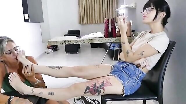 Older woman kissing tattooed young woman's bare feet, worshiping sneakers socks