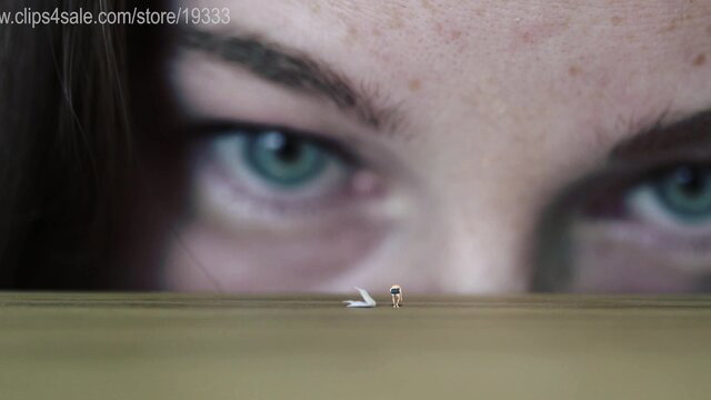 Giantess with piercing green eyes peers down at tiny man on vast plain