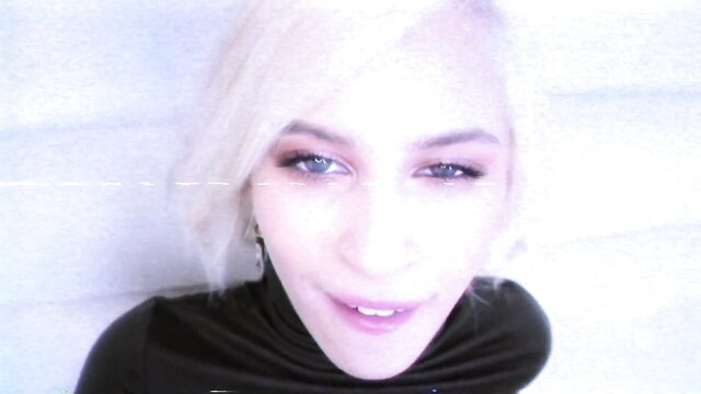 Blonde Kiara Cole smirks seductively in neon-lit closeup