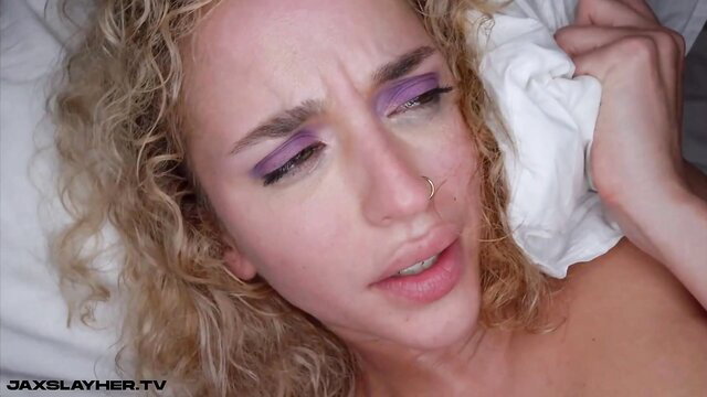 Blonde with purple eyeshadow crying, wiping face with cloth in bed, nude