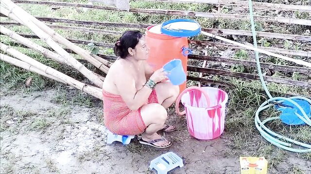 Asian MILF squatting nude outdoors pouring water in outdoor bath