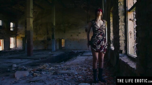 Blindfolded redhead in floral dress stands in abandoned warehouse