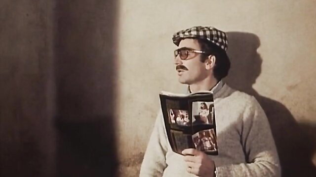 Handsome 70s man in checkered cap and sweater holds porn mag thumbnail