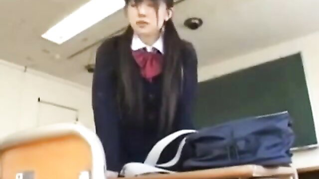 Japanese schoolgirl in uniform stands over desk in classroom tease
