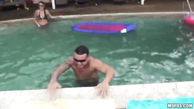 Tattooed Latino hunk climbing out of pool at hardcore party, sexy bikini babe watches