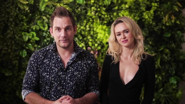 Hot blonde and handsome guy in deep V-neck dress, green wall interview tease