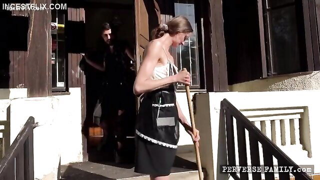Blonde in sexy maid outfit holding broom on porch with man behind
