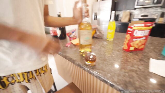 Black guy in yellow shorts pours whiskey in kitchen, amateur thumbnail