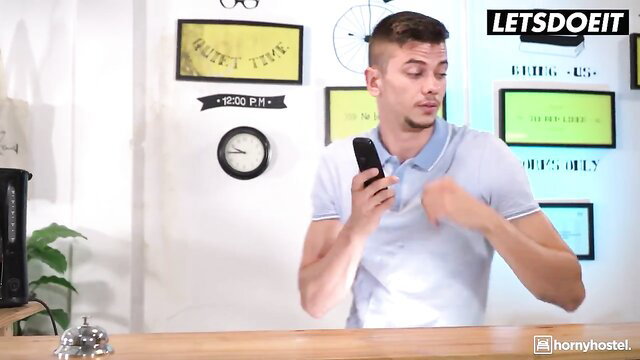 Handsome young man flexing muscles at hostel desk in tight polo shirt