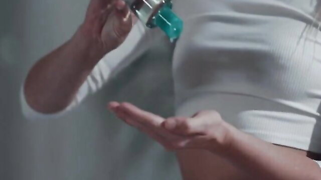 Blonde Kenna James applies green lotion on hand in tight white crop top