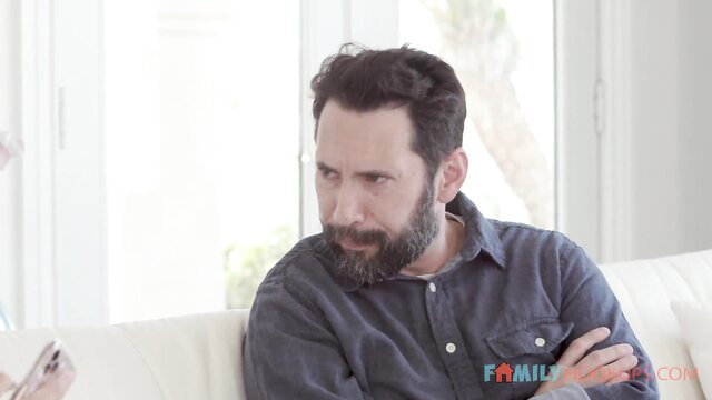 Handsome bearded man in chambray shirt on sofa, thoughtful gaze