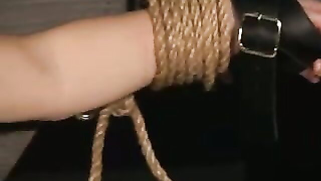 Woman bound with ropes and leather straps on arm in crucifixion fetish scene