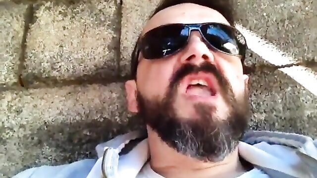 Bearded handsome guy in shades smoking and stroking on stone ground