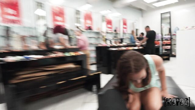 Brunette bent over black couch in shoe store, tank top slipping off