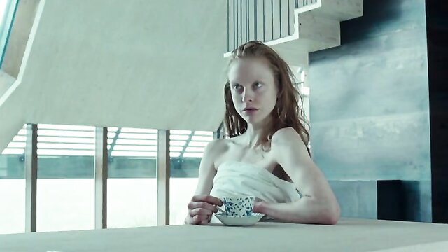 Woman sitting at a table with a cup, topless and wrapped in a sheet