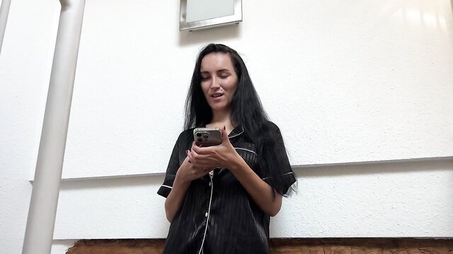 Hot Asian stepmom in black satin pajamas holds phone, seductive smile