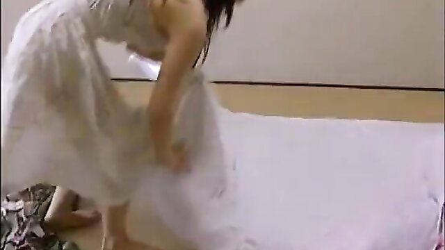 Japanese woman in white dress bending over bed in JAV family sex scene