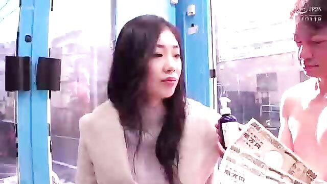 Asian woman in beige sweater with nude man holding cash in JAV booth scene