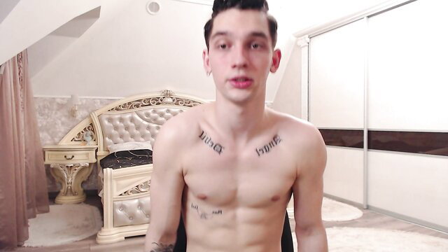 Shirtless twink Teddy_mode with chest tattoos sits nude on bed