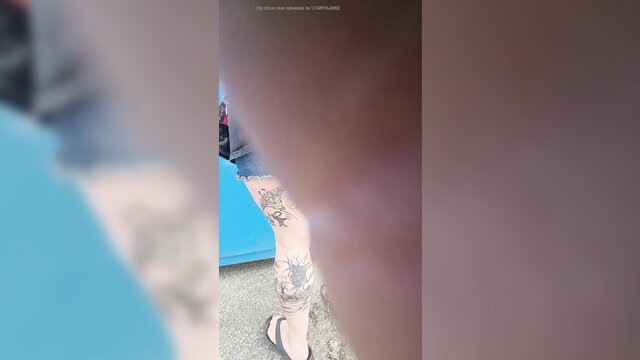 Blurry closeup of woman's tattooed leg in high heels by blue porta potty