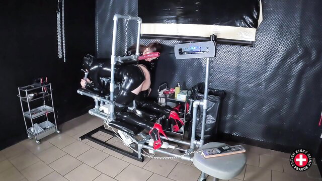 Shiny latex-clad sub bound in gyno chair for robo-fuck torment