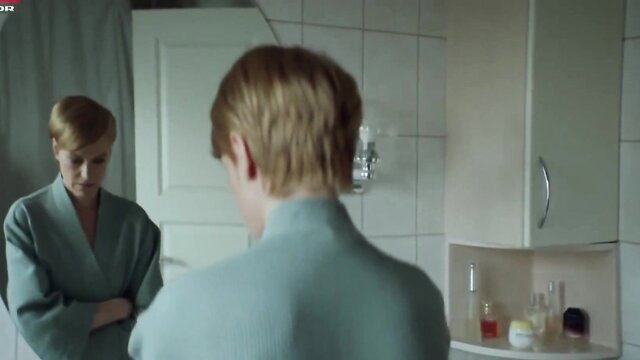 Maria Rich in bathrobe, blonde bob haircut, bathroom mirror scene from Bedrag