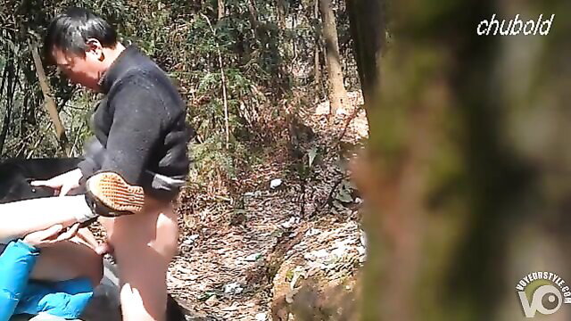 Mature Asian man nude outdoors in woods with partner hand on cock