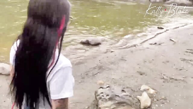 Katty Blake in white tank top by river, long black red streak hair