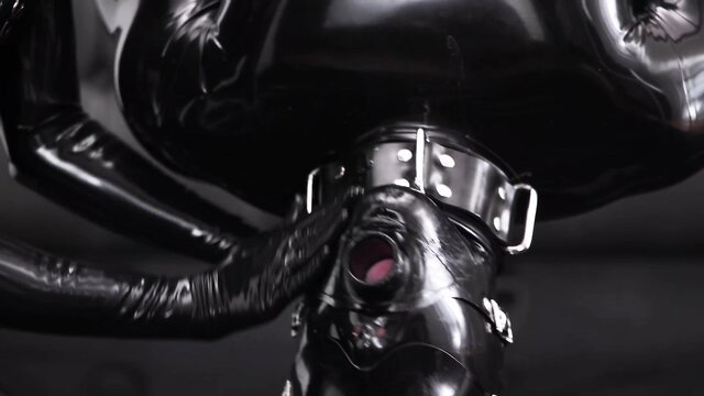 Shiny latex fetish domme in gas mask with open mouth, glossy black catsuit