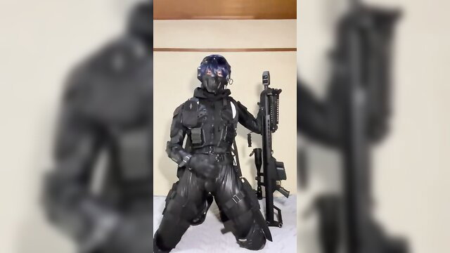 Cosplay sniper in tight black latex suit kneels with rifle, teasing crotch bulge